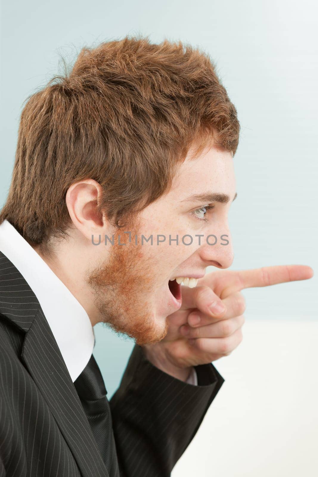 Close-up side portrait of young man with short red hair and beard in suit and tie. Funny expression, he smiles pointing to the left (in front of him), as if to point or accuse by saying 'ah-haa! then