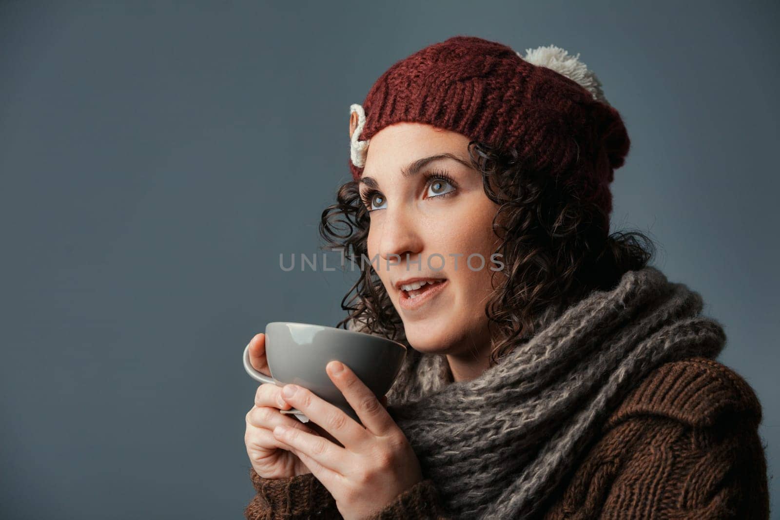 Embraced by winter, a woman in woolen attire sips a comforting drink like milk, café latte, or chocolate. Settled in a mountain retreat or café, she gears up for errands with her vivid eyes gleaming