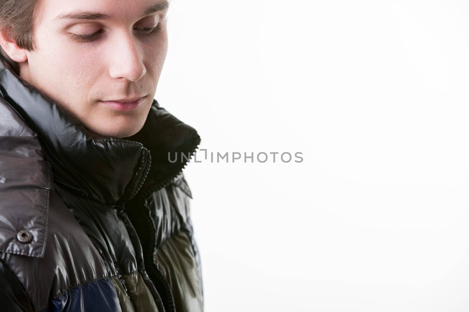Dressed in a black puffer jacket, a young man exudes mystery and charm, his eyes shyly looking down. Symbolizing winter style, warmth, and male attractiveness. Generous COPYSPACE on the right