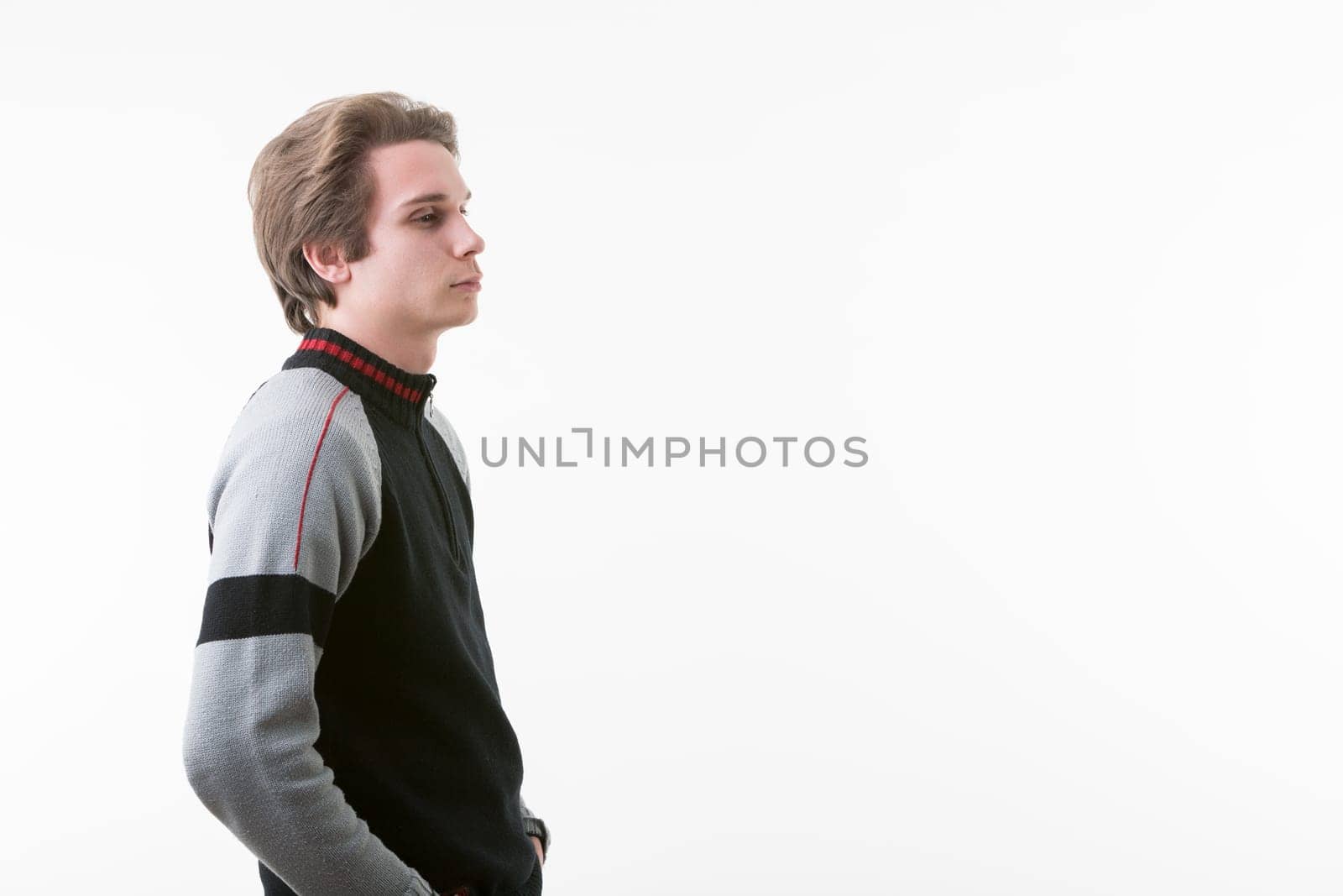 young man in a black, gray, and red-striped sweater stands with hands in pockets, gazing toward the COPYSPACE on the right. With a slightly sporty, wintry look, his light brown hair is short, and he w