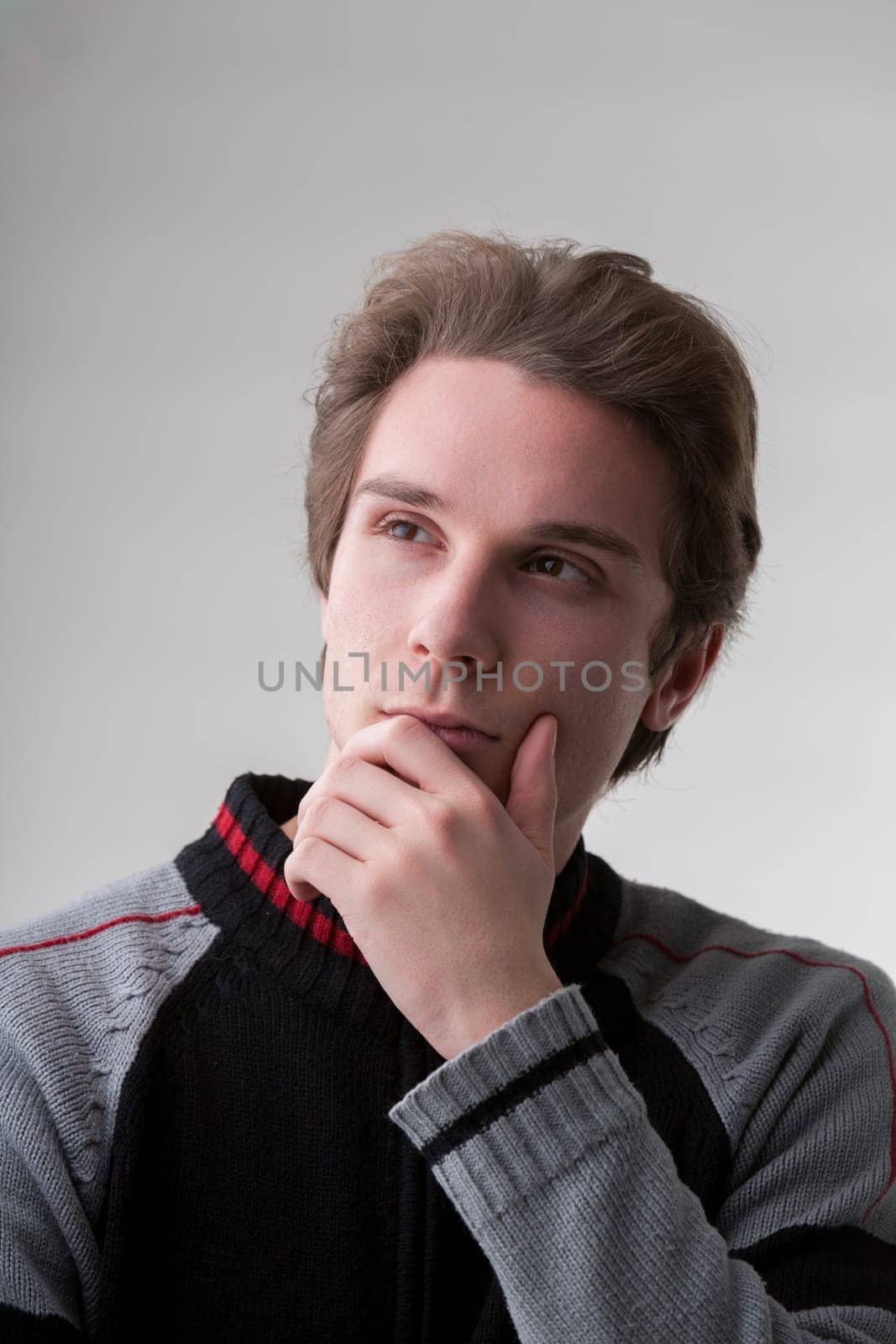 Wearing a black and gray sweater, a charming man with short light brown hair contemplates deeply, looking upward. His expression suggests he's come to a significant understanding or has a promising id
