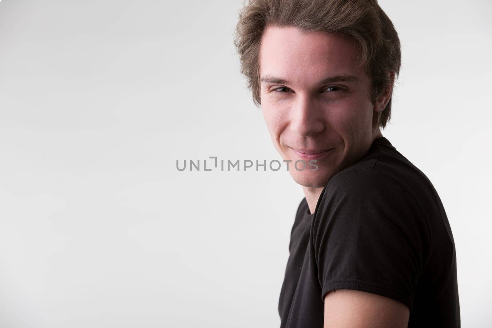 On a neutral background stands an attractive young man in a black tee, his brown hair short. His intense eyes and smile suggest deep opinions and skills