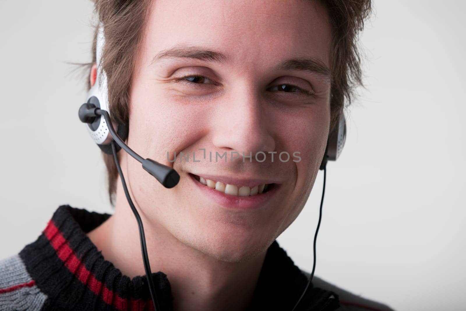 friendly young call center man answers clients' calls with a smile, embodying the company's promise of excellent customer service. Wearing a black and gray sweater and a professional headset