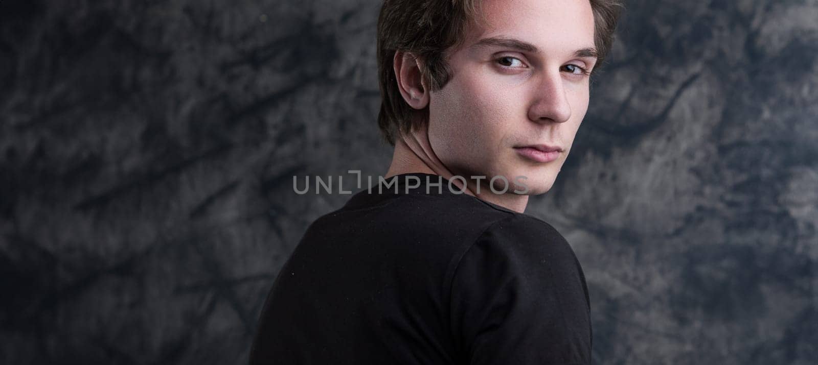 light-brown-haired man, in a black shirt, stands thoughtfully before a grunge blackboard. His introspective gaze offers ample COPYSPACE for content