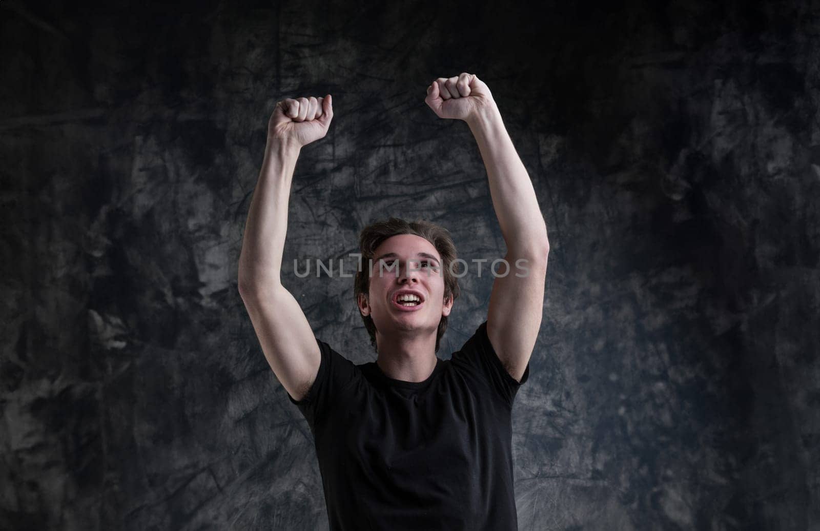 Victory is clear on a young man's smiling face. Light-brown hair, black shirt, with arms uplifted, he symbolizes success against grunge