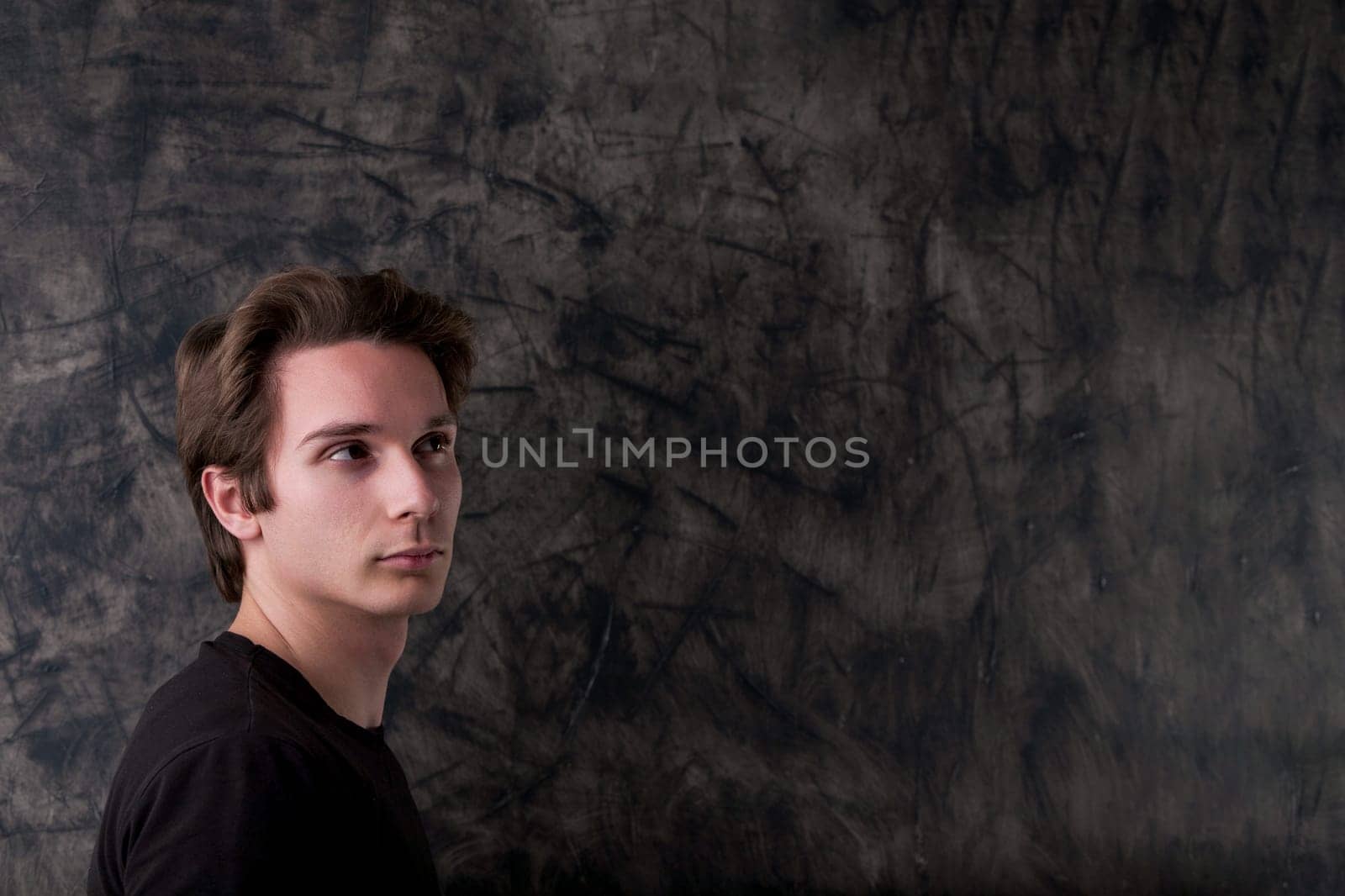 In a black t-shirt, a man stands pondering in front of a wiped chalkboard, signifying an upcoming brilliant idea. Ample copyspace for your input