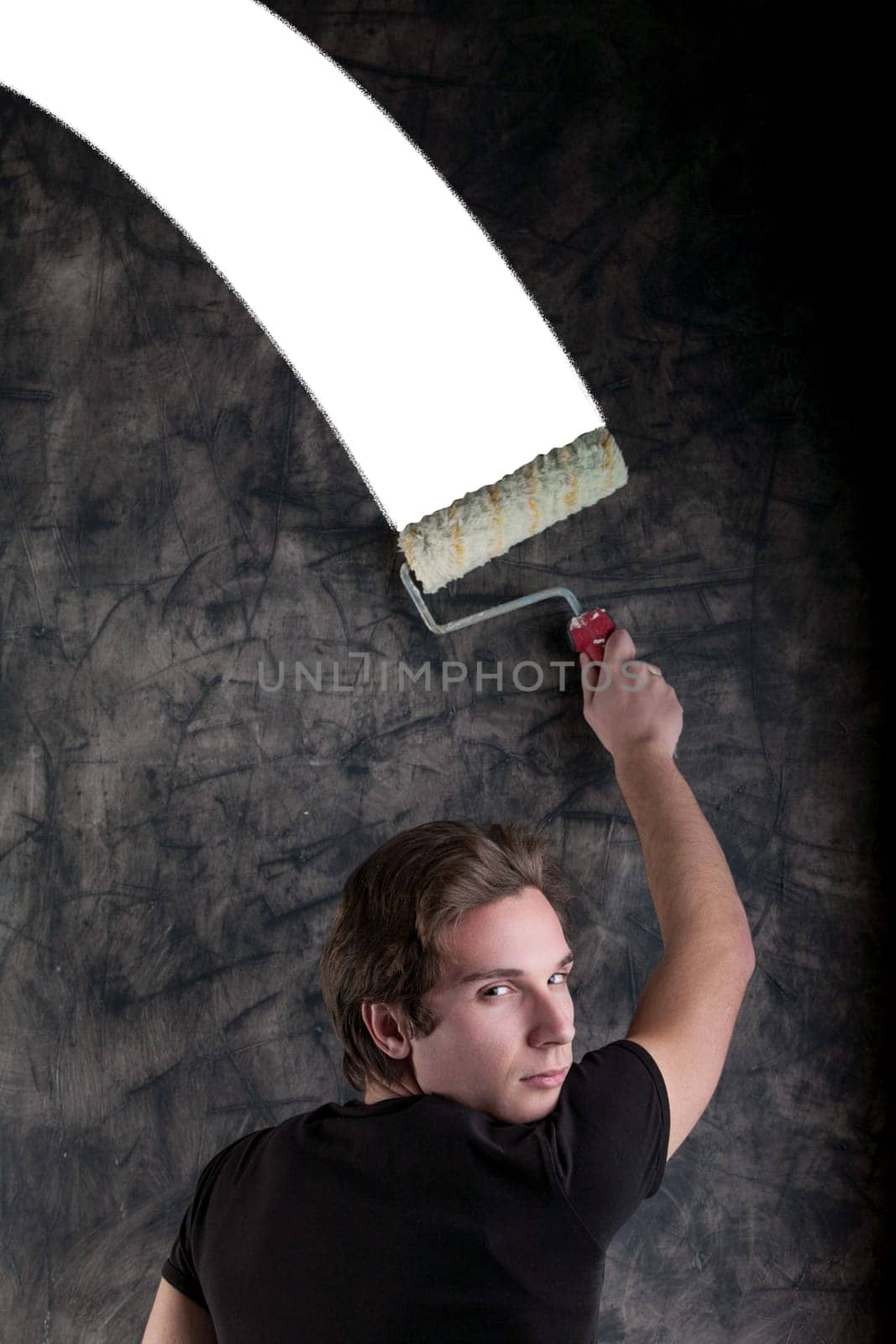 On a black grunge-marked board, a dashing youth with light-brown hair in a black tee uses a roller to craft a perfect white section intended for COPYSPACE