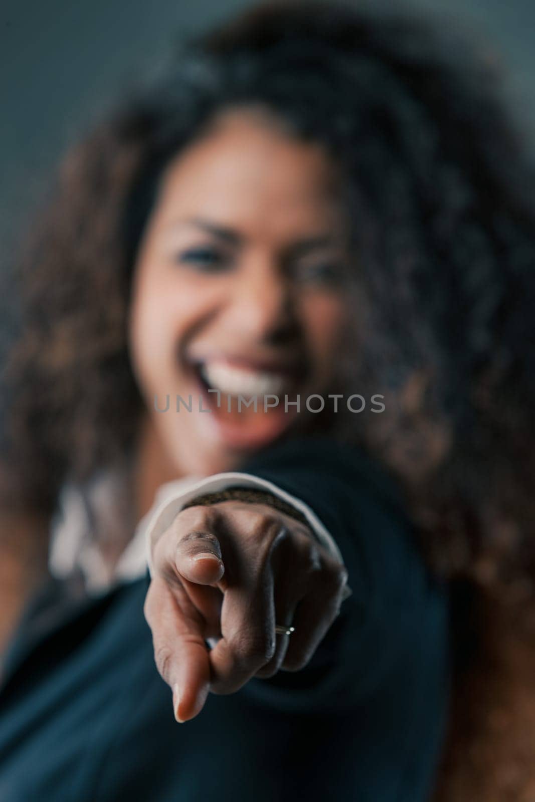 The sharp focus on the pointing finger of a radiant black woman contrasts with her blurred background. Long hair and dark dress frame the ideal space for COPYSPACE