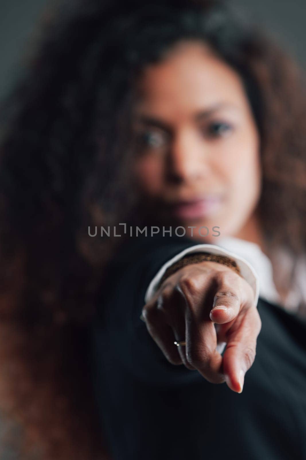 Beautiful Woman with black skin and long wavy hair, elegant blurred in the background. In focus her outstretched index finger pointing toward us, choosing us.