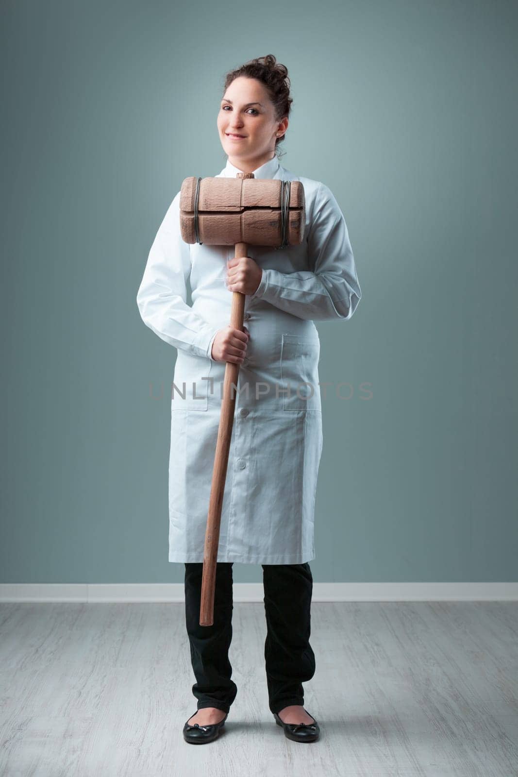 Humorously exaggerating, a scientist in a white coat, inside a blue-green room, swings a 20 KG wooden hammer. It symbolizes the potential danger of not upholding rigorous, independently verified scien