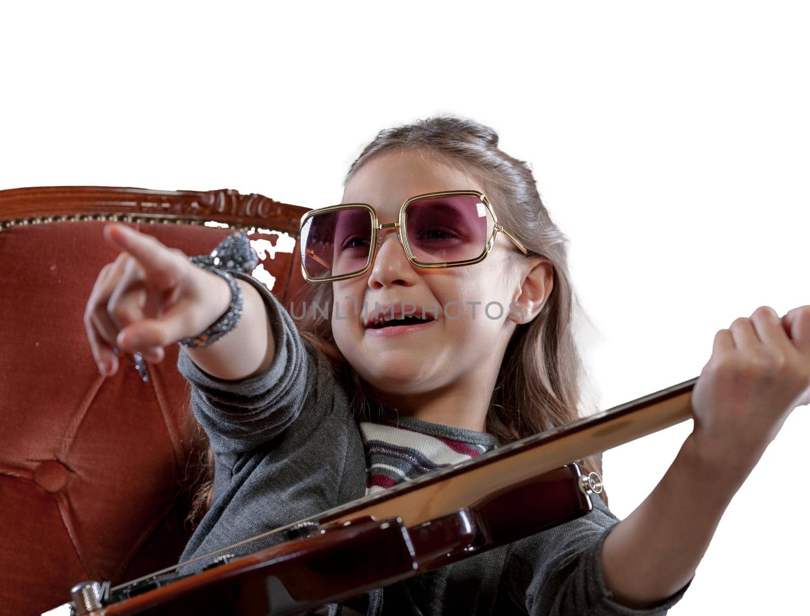 In her own concert, a young girl with an electric guitar, sunglasses, engaging an imaginary audience from her velvet baroque armchair