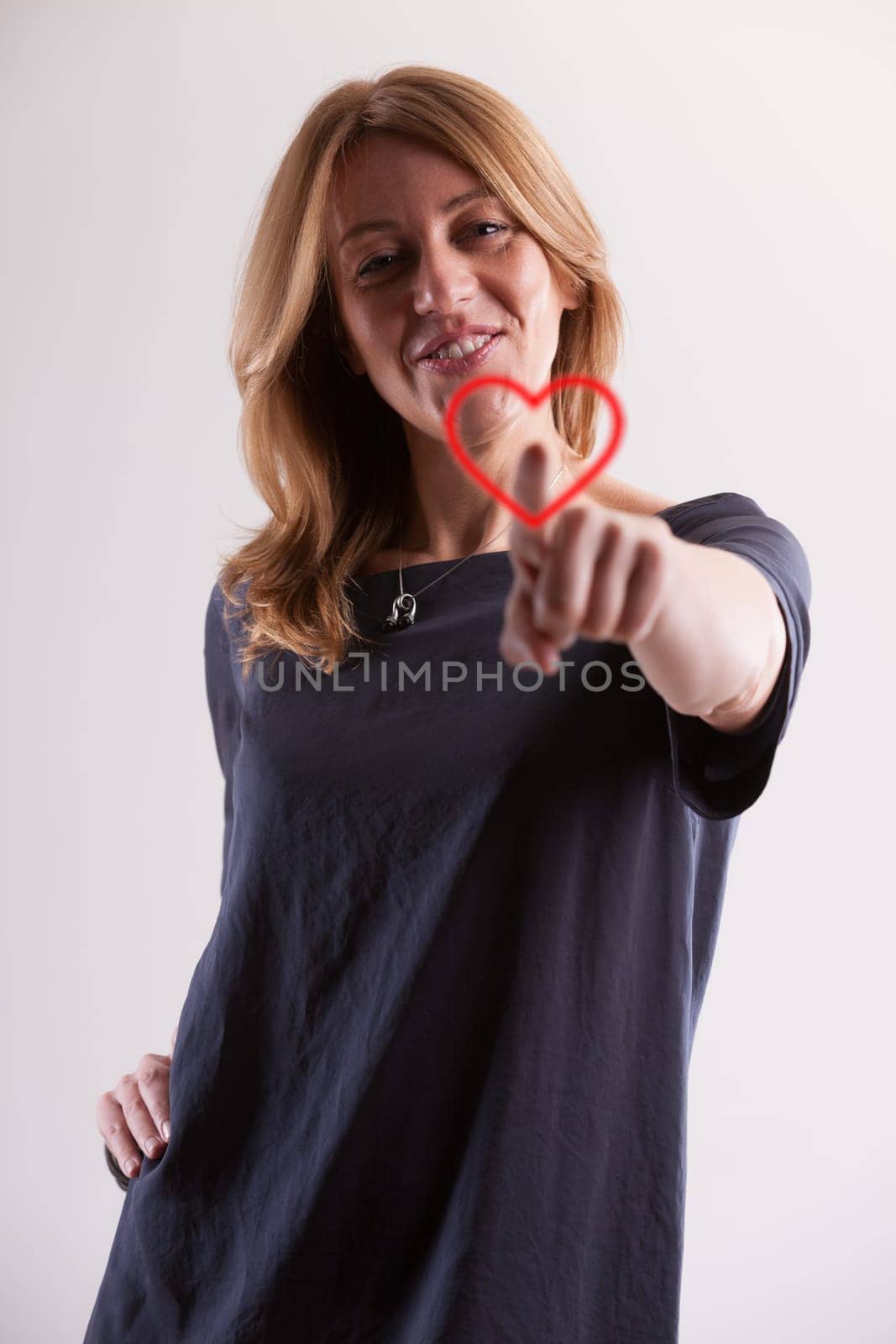 radiant blonde woman around 40, with fair skin, joyfully touches a symbolic heart image. As age demands greater cardiovascular care, love, too, matures and can be cherished more deeply, even on Valent