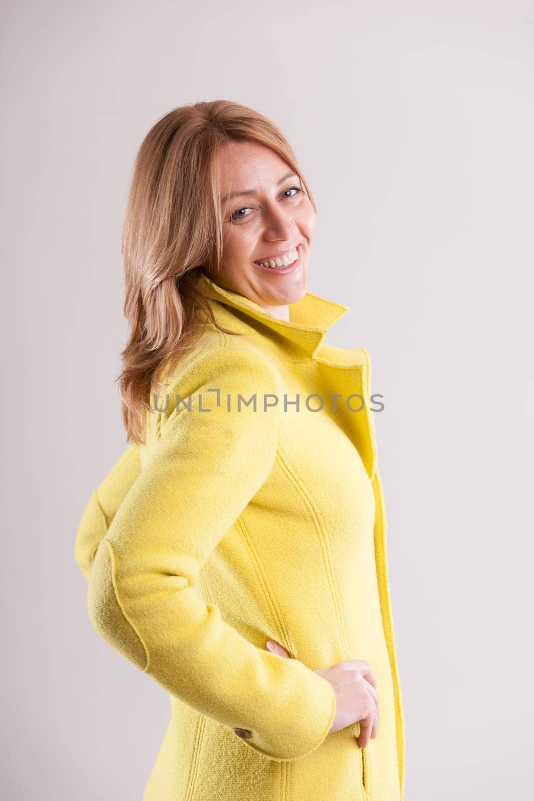 merry adult woman clad in a yellow coat shows off a flirtatious smile. Her portrait stands out against a muted background