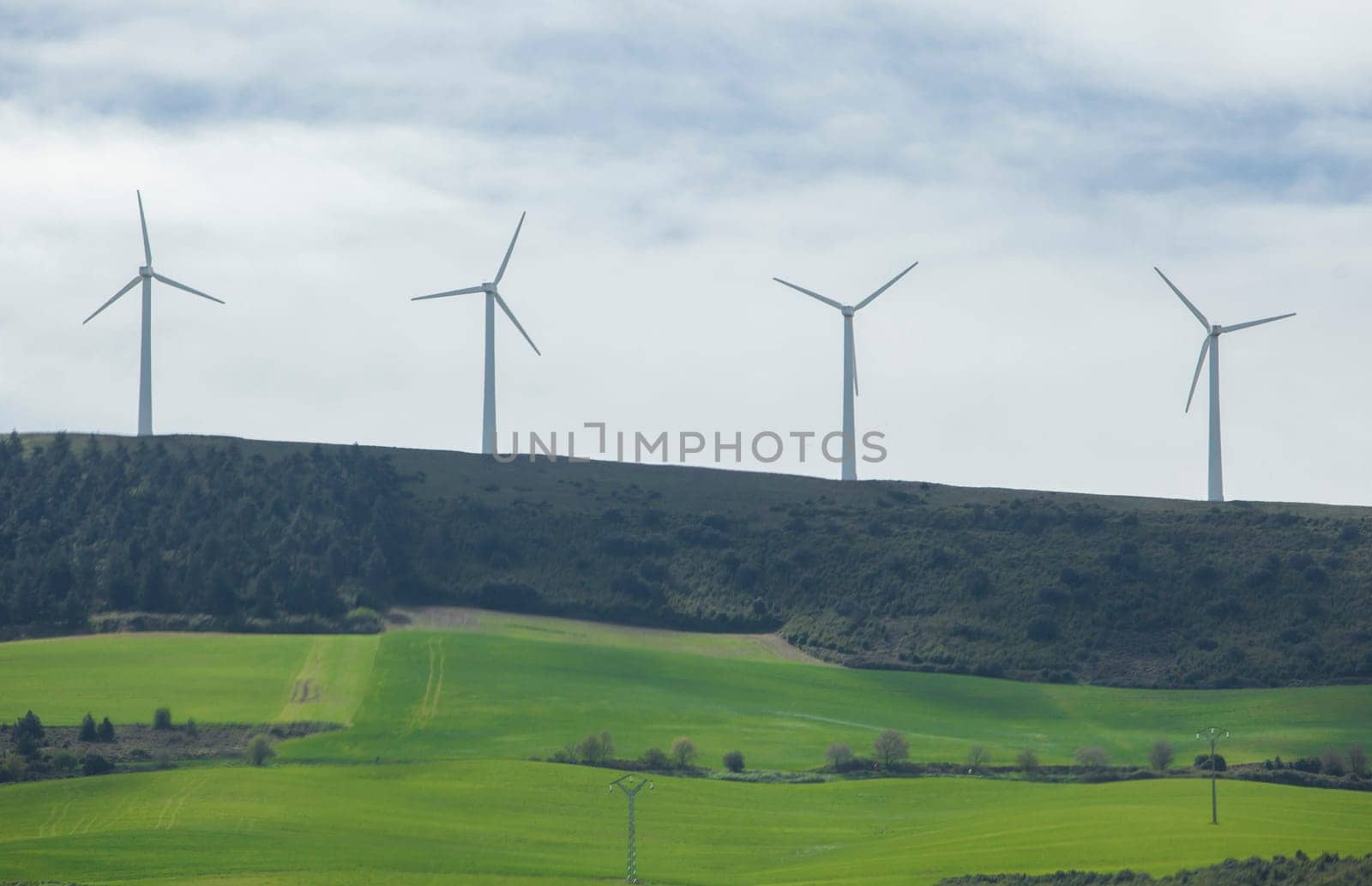 Wind turbines on the top of the hills. Green meadows at the foot of the mountain
