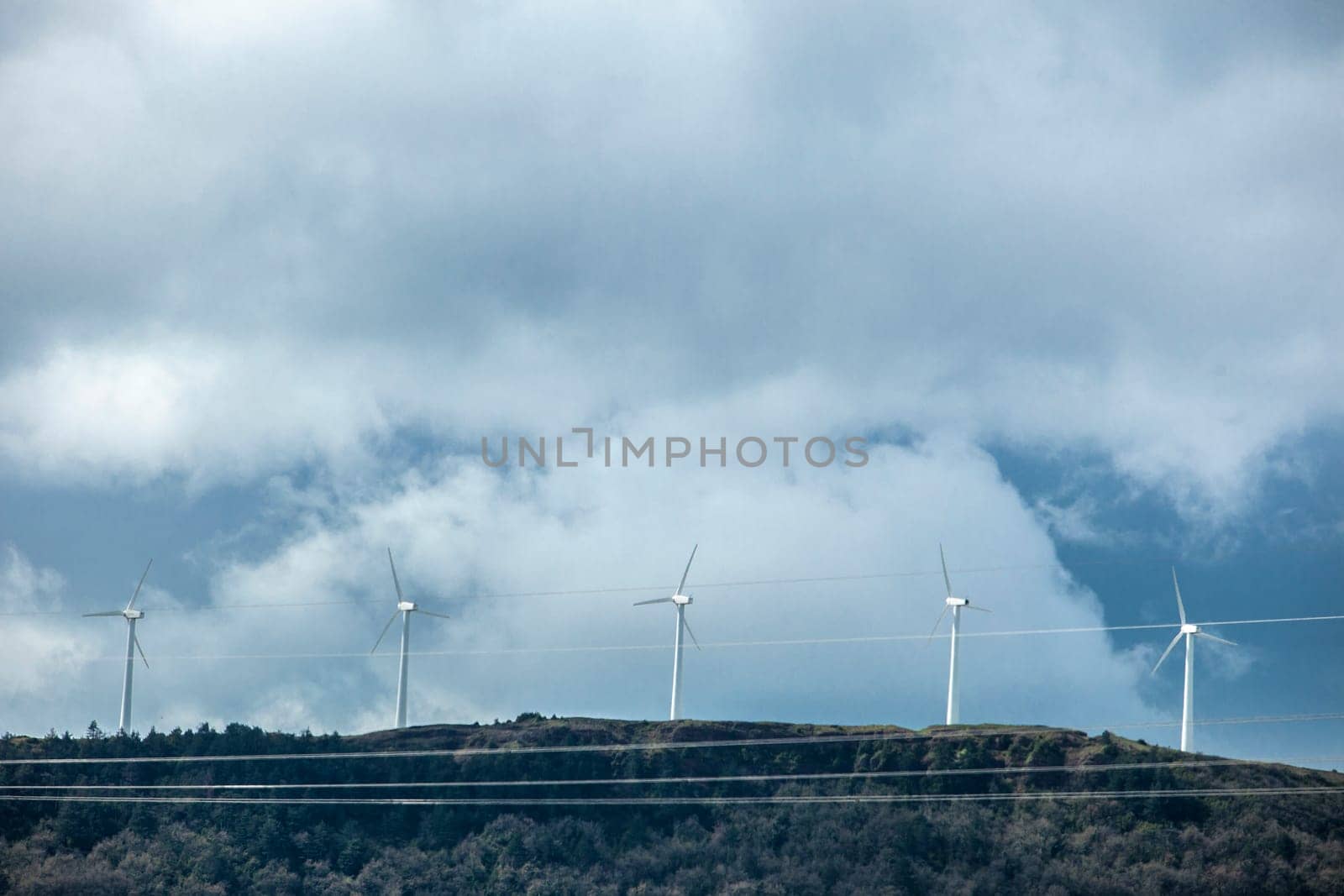 Wind turbines on the top of the hills. Power lines in the foreground