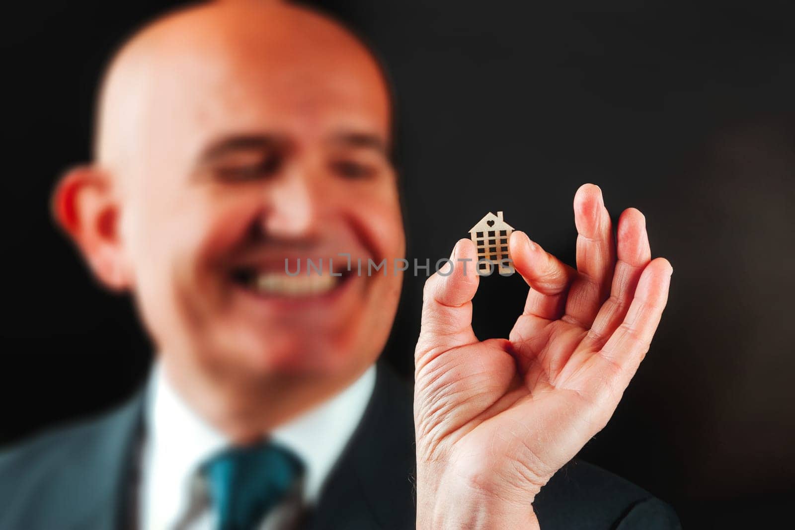 Holding a small emblematic house, a cheerful bald senior reflects every human's foundational ambition: owning property, protecting it with financial wisdom, and enhancing life step by step
