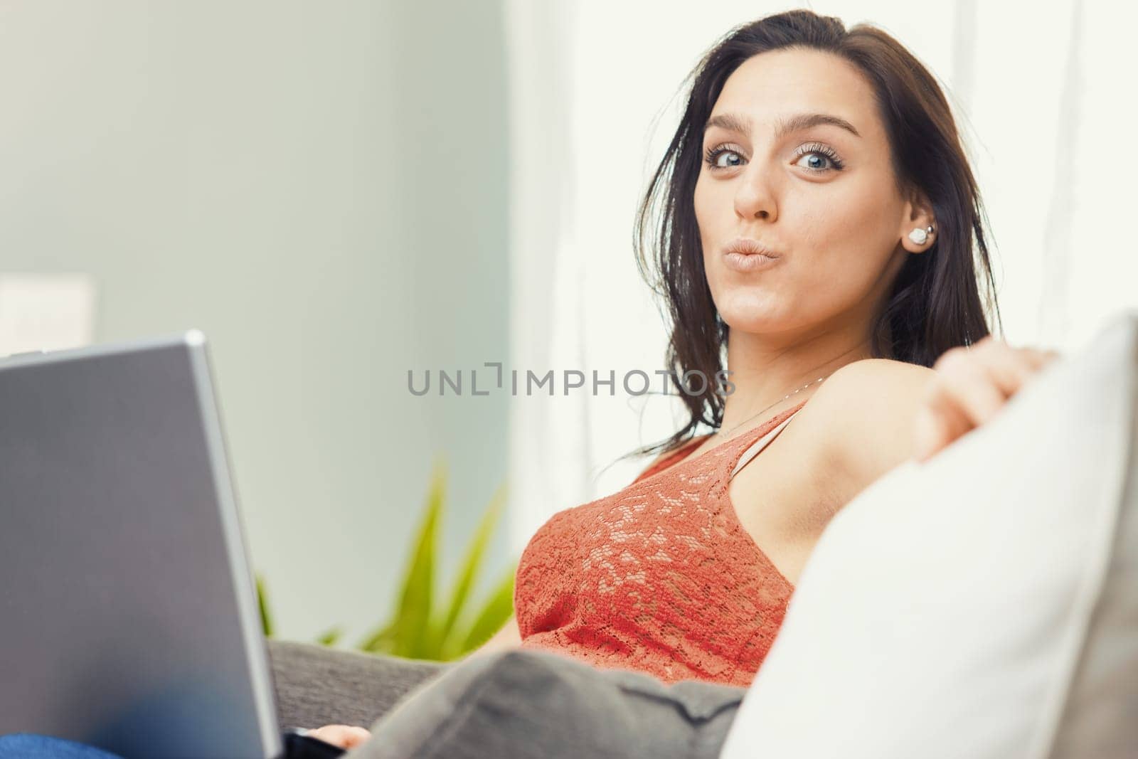 A woman wearing a red lace tank top is busy using her laptop at home. Comfortably on the couch, she can work efficiently without the annoying pressure of the office environment. It's either this or th