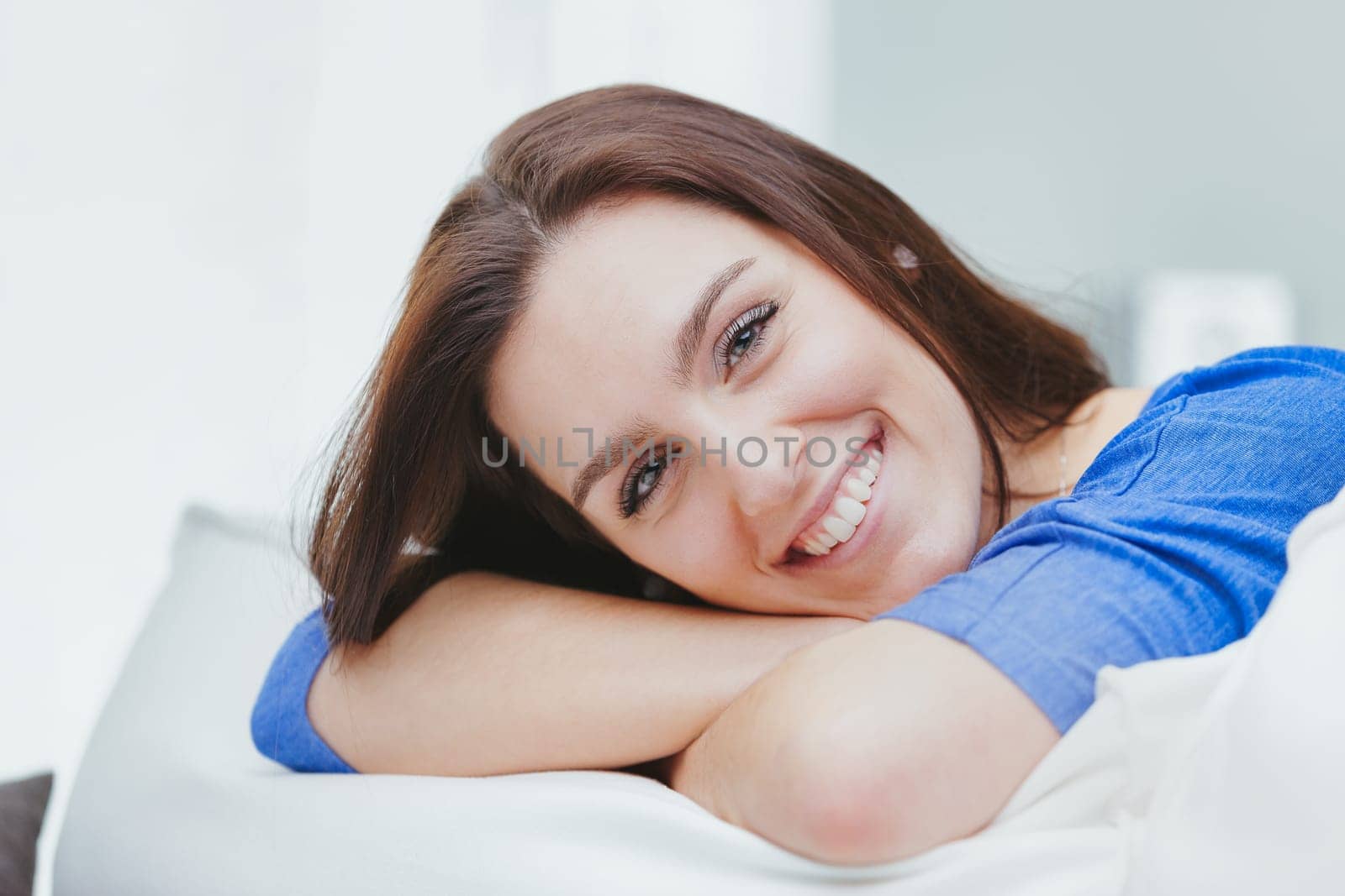 A young, happy, and dreamy woman smiles with her head resting on her crossed arms, which are in turn leaning against the cushion of the sofa. She imagines, invents, and reasons. She imagines a way to