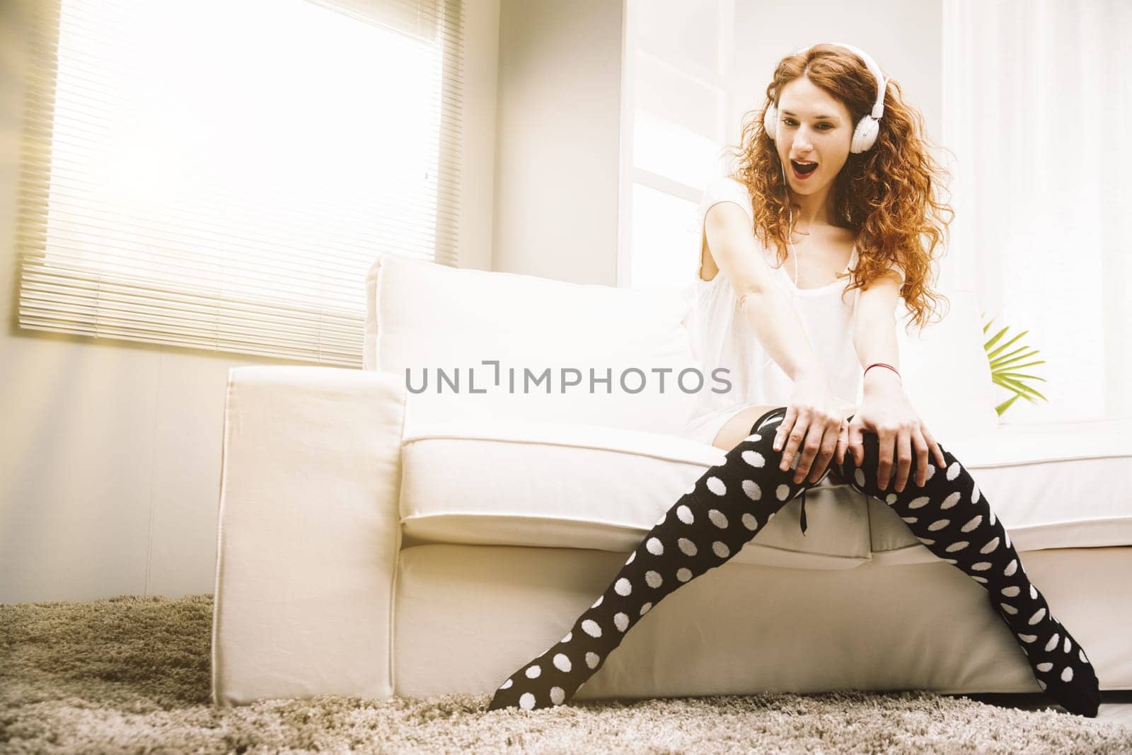 In her bright home, a young, slender woman with striking red hair loses herself in music. Dressed casually, she sits on a white couch, indulging in the rhythms from her white headphones