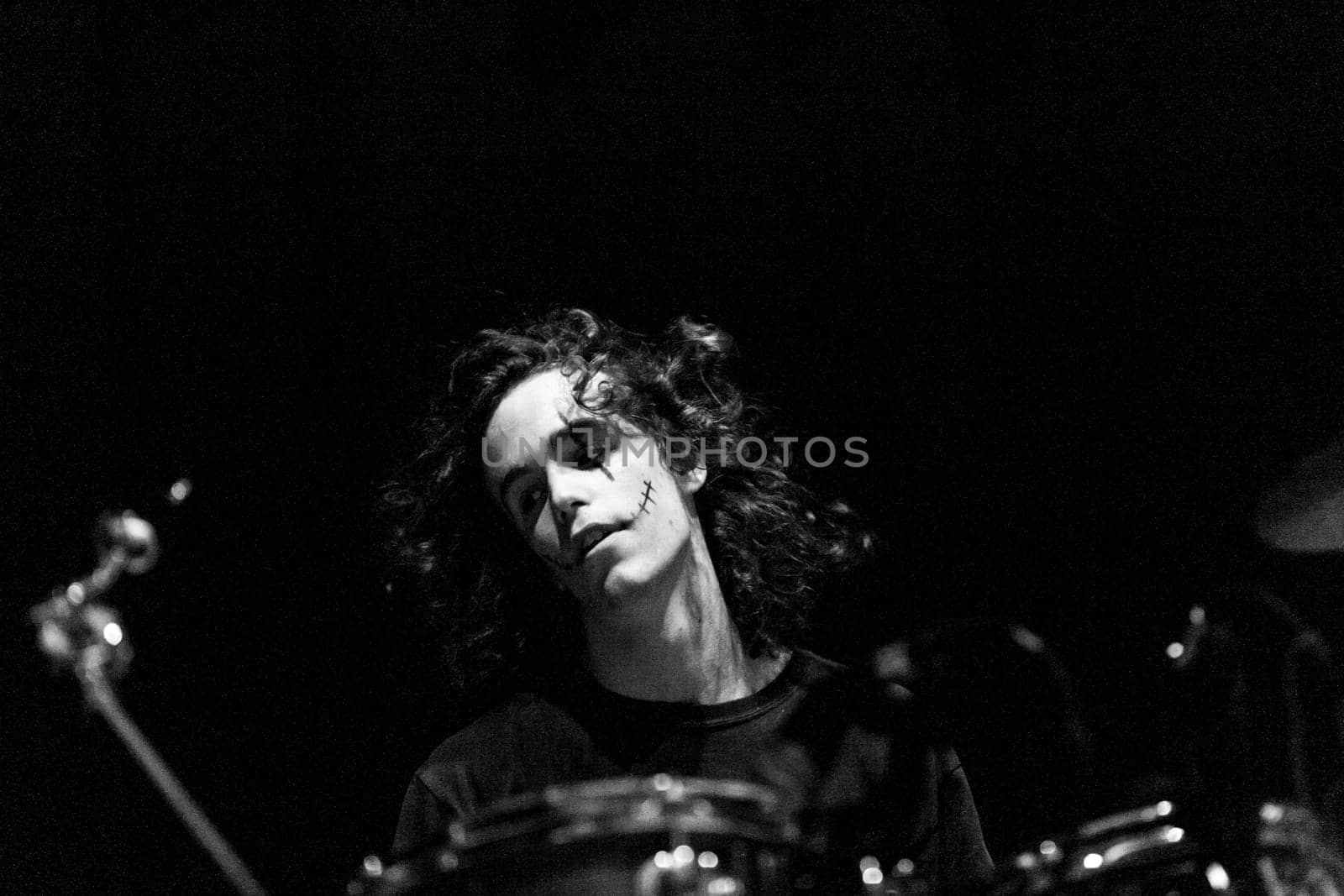 Captured in black and white, a drummer with dark makeup loses himself in the fervor of live music, exuding the essence of a true rocker with every move
