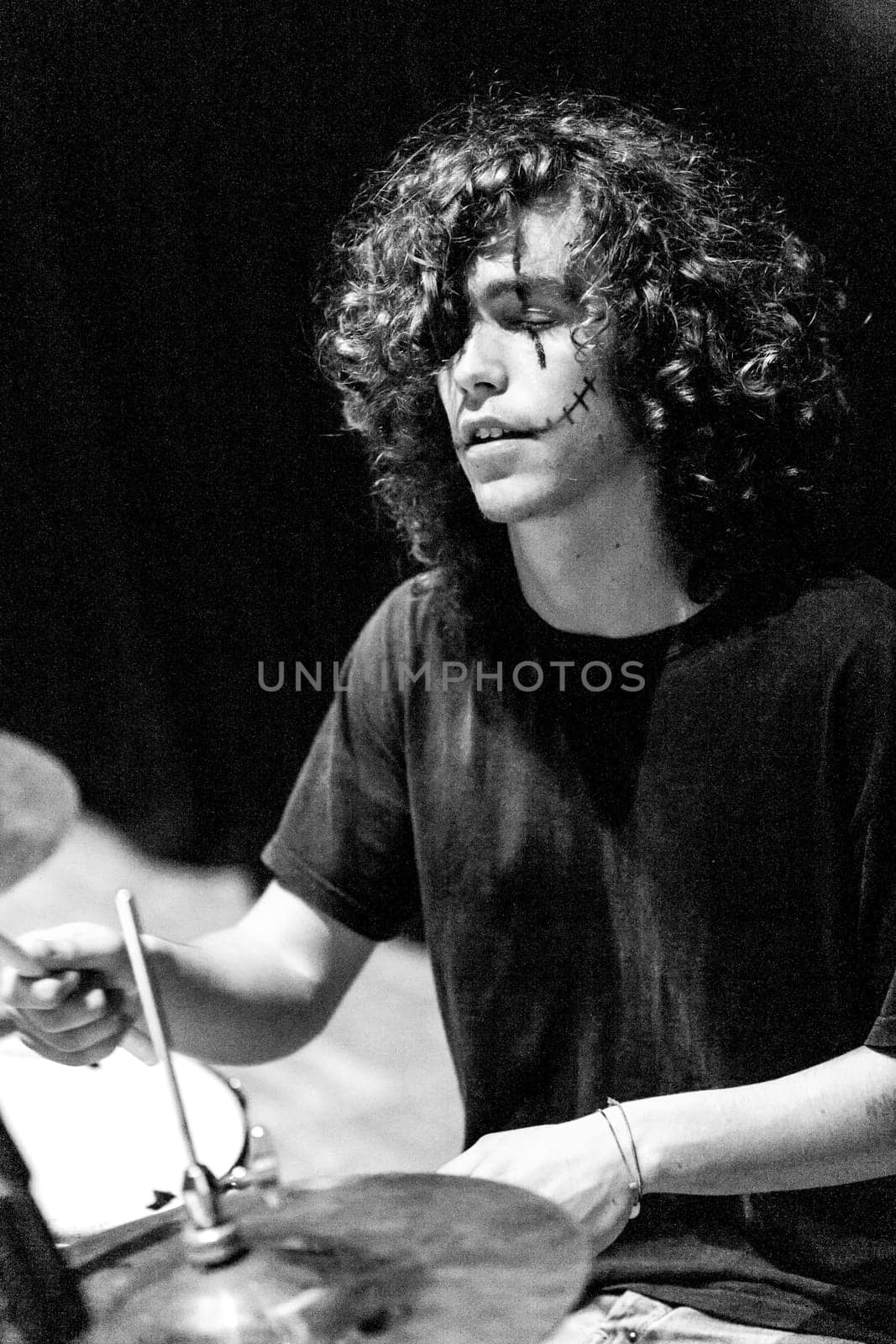 Lost in a musical trance, a drummer with a rocker's essence performs live. Dark makeup frames his face, embodying the juxtaposition of control and release