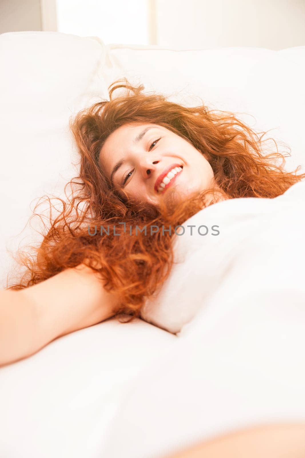 The sheer softness of a white sofa mesmerizes a radiant redhead, drawing a comparison to a bed's coziness. Her genuine smile depicts her living room's sheer luxury and comfort