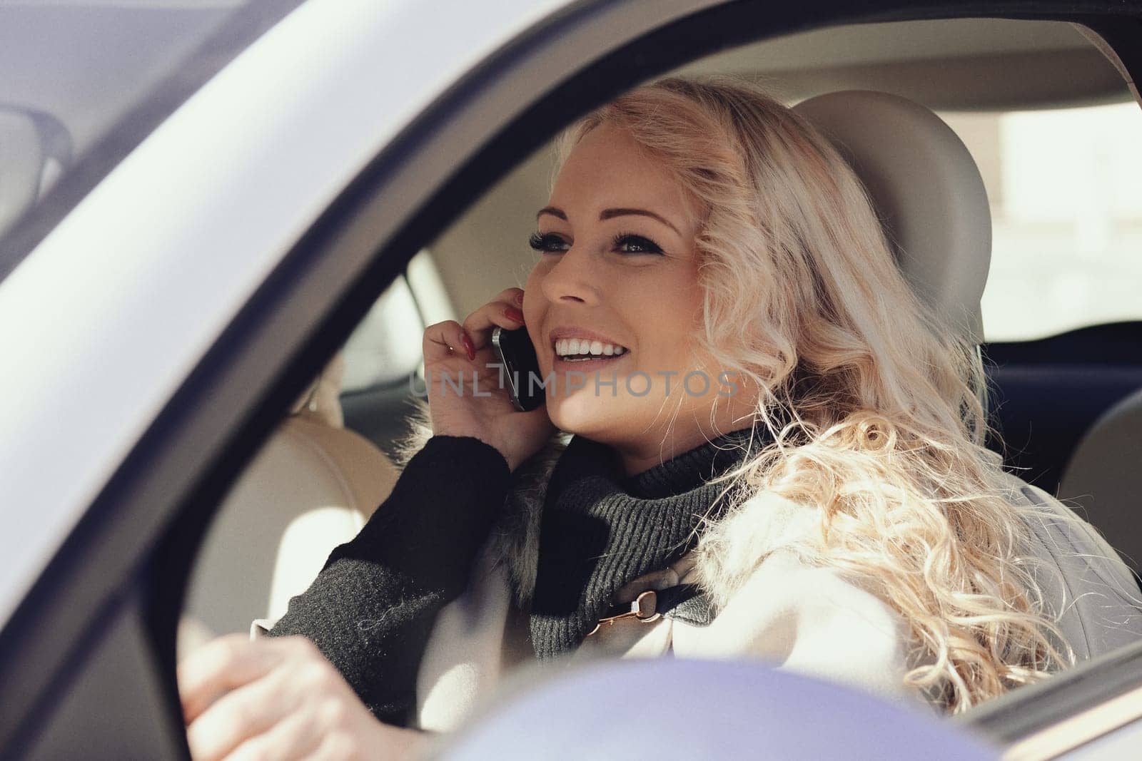Beautiful young blonde woman with long hair, very outgoing, uses her phone and smartphone while driving a fashionable small car in Europe, about to have fun with friends or as an independent tourist,