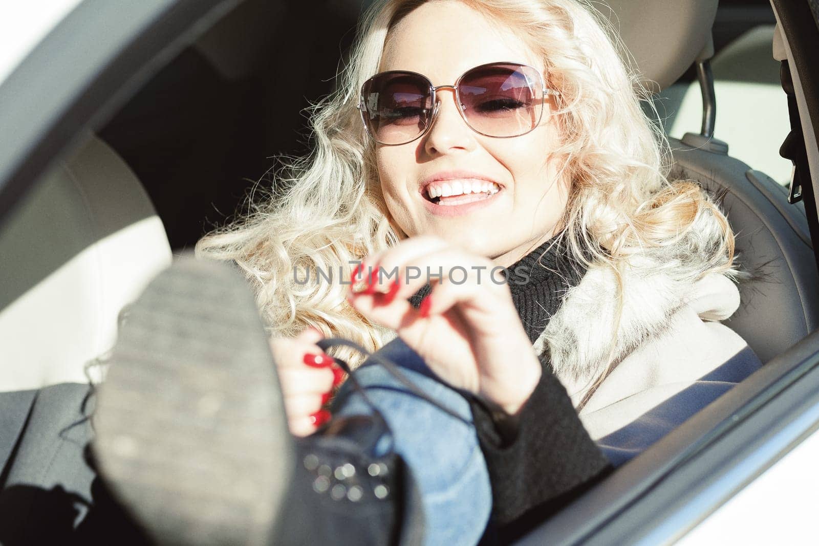 Polish tourist leans her foot out the window of her car to lace up her boots as a showbiz star or fashion influencer would. The blond girl smiles and has a lot of makeup on.
