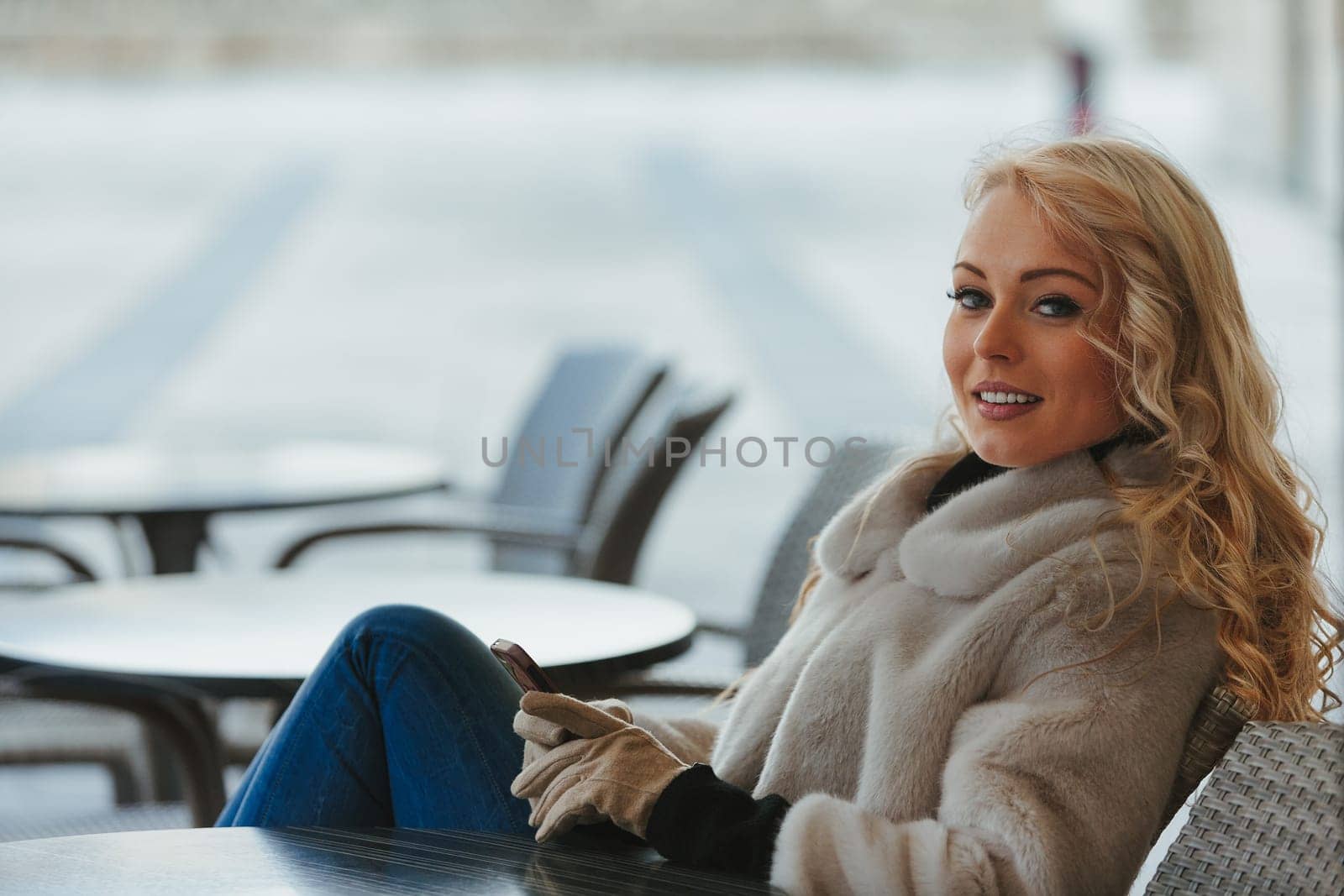Beautiful young blonde woman sitting at a bar, having fun, laughing at something hilarious on her smartphone or a received message. She's a tourist in a European city, enjoying the fresh air, dressed