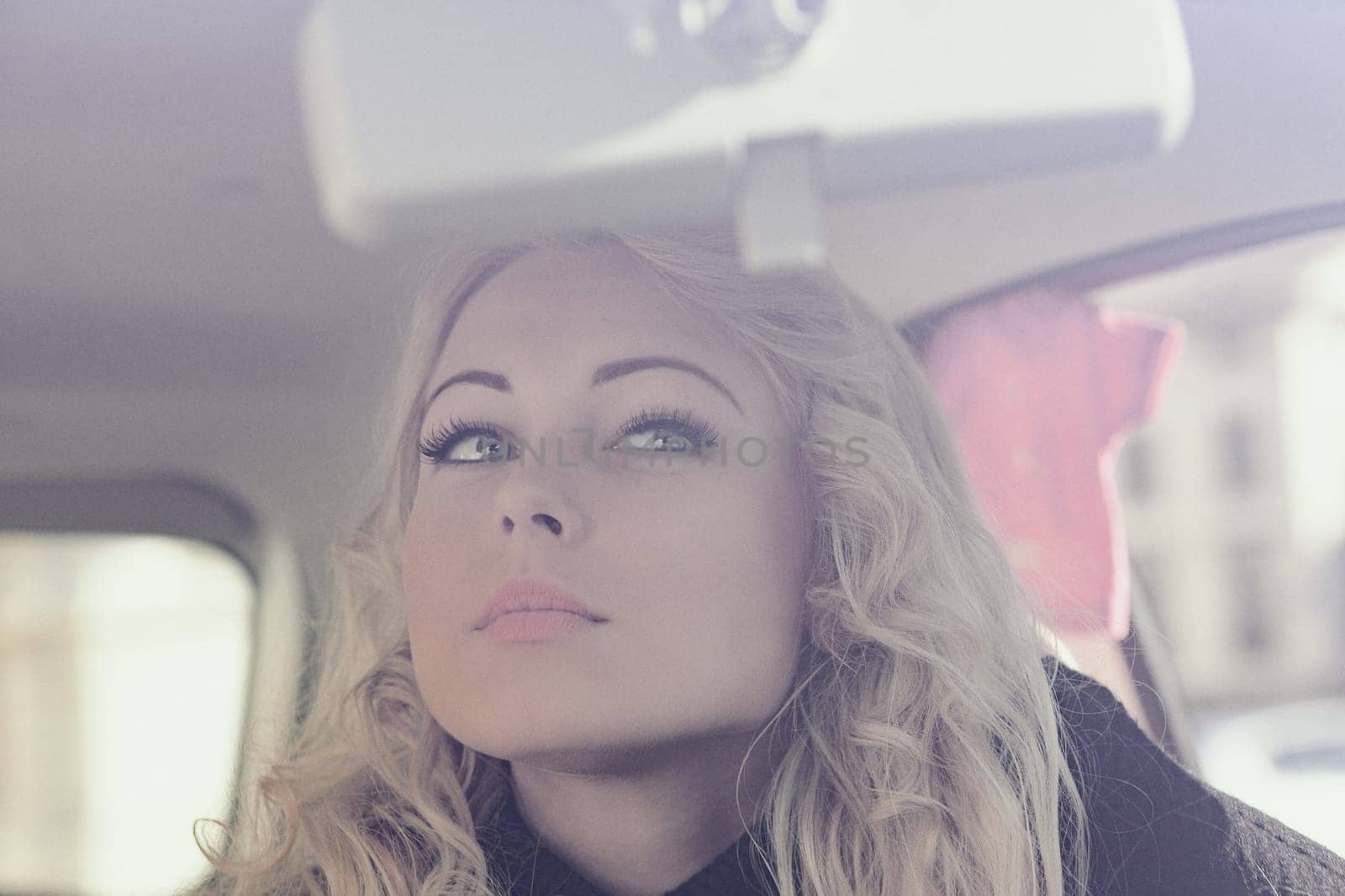 A blonde woman is touching up her makeup or applying it in her car. She is stunning and wants to be perfect for herself and a potential date tonight. She's not a prey but a hunter