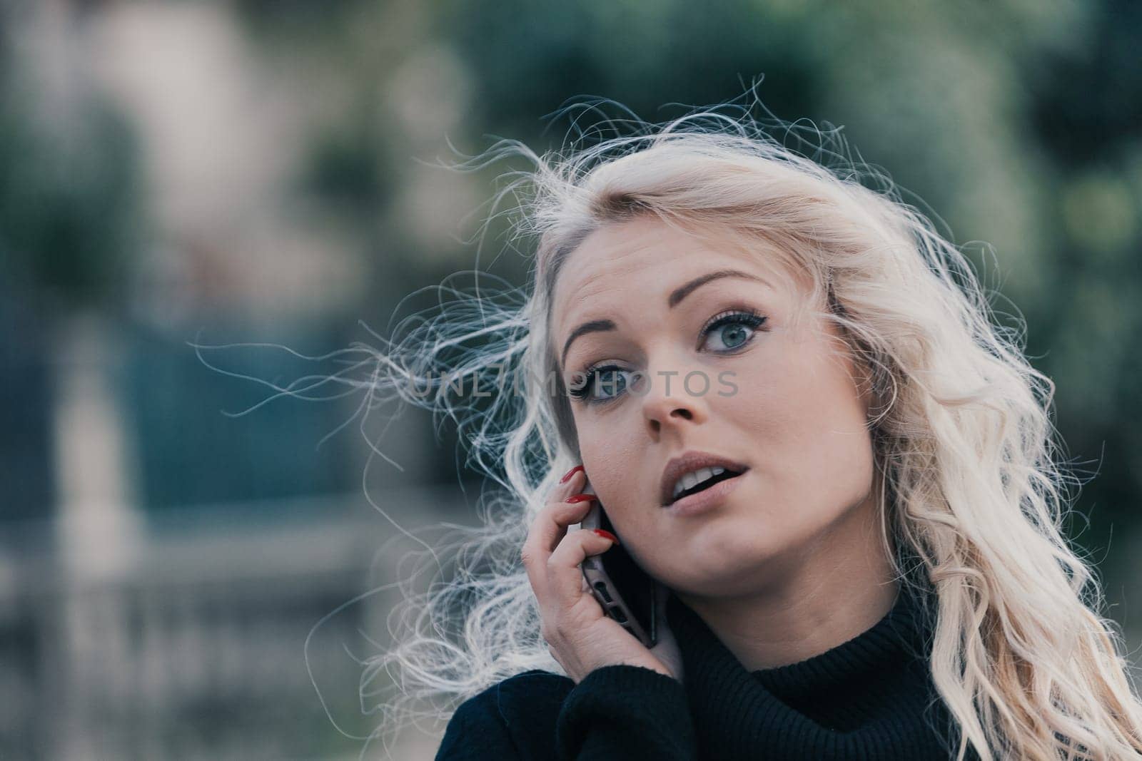 Young woman with long, curly, perfectly permed blonde hair, perfect makeup and manicure, is a tourist in a European city with medieval villages. Using her phone to talk, chat, or access Wi-Fi for hist