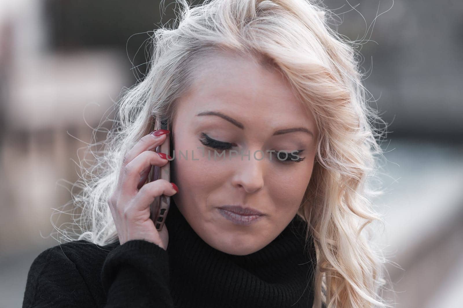 Young woman with long, curly, perfectly permed blonde hair, perfect makeup and manicure, is a tourist in a European city with medieval villages. Using her phone to talk, chat, or access Wi-Fi for hist