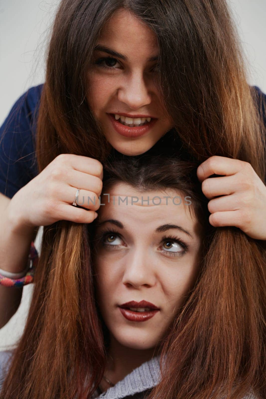 Friends or sisters, two young women with pristine makeup and hair, indulge in playful antics. Their cheerful expressions and jests speak of pure, unburdened joy