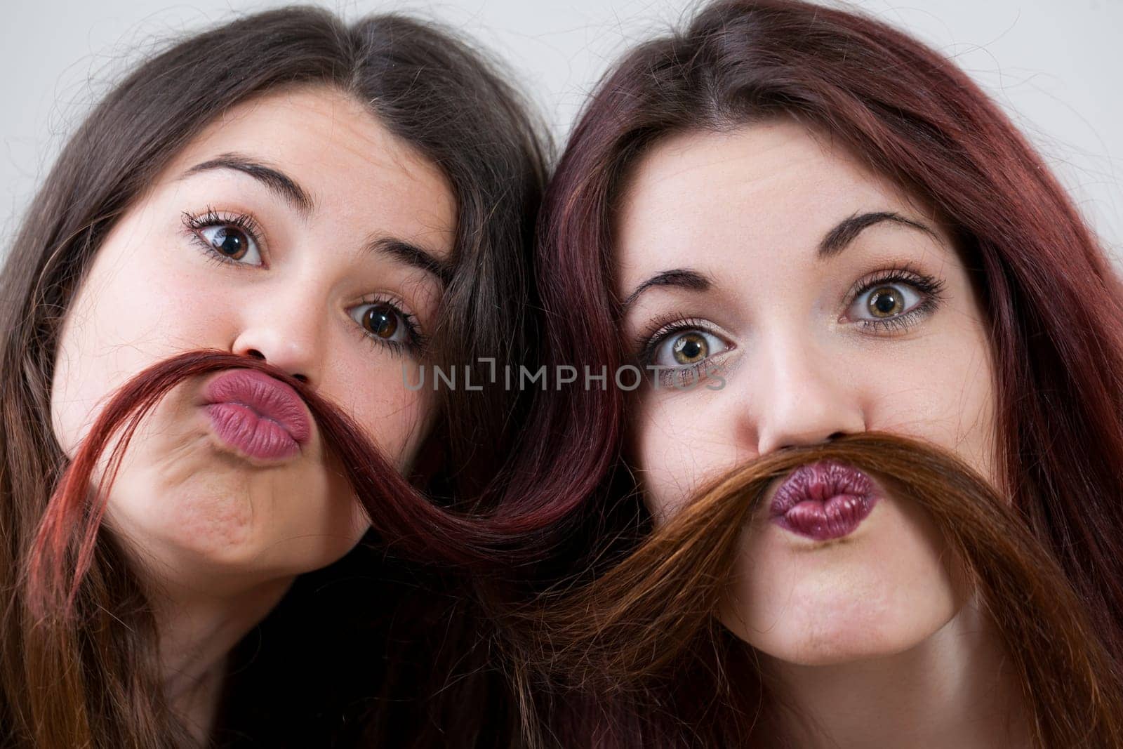 Carefree and radiant, two young women with impeccable makeup and hair, capture the spirit of youth, making hilarious faces, and having a blast