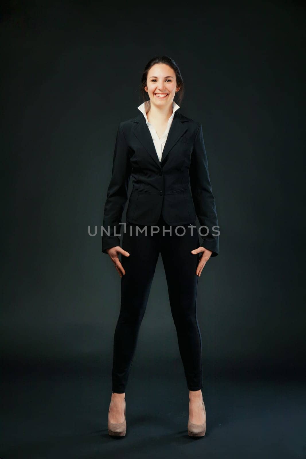 Woman in black, standing on black background. Wears heels for self-love, not submission. Her hard work and professional commitment bring her satisfaction, not just luck