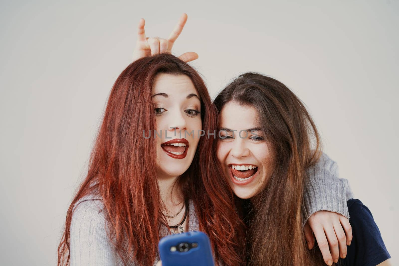 Perfectly groomed yet playful, two young women make amusing faces, possibly for selfies or at a mirror. Their laughter and odd hair antics are infectious