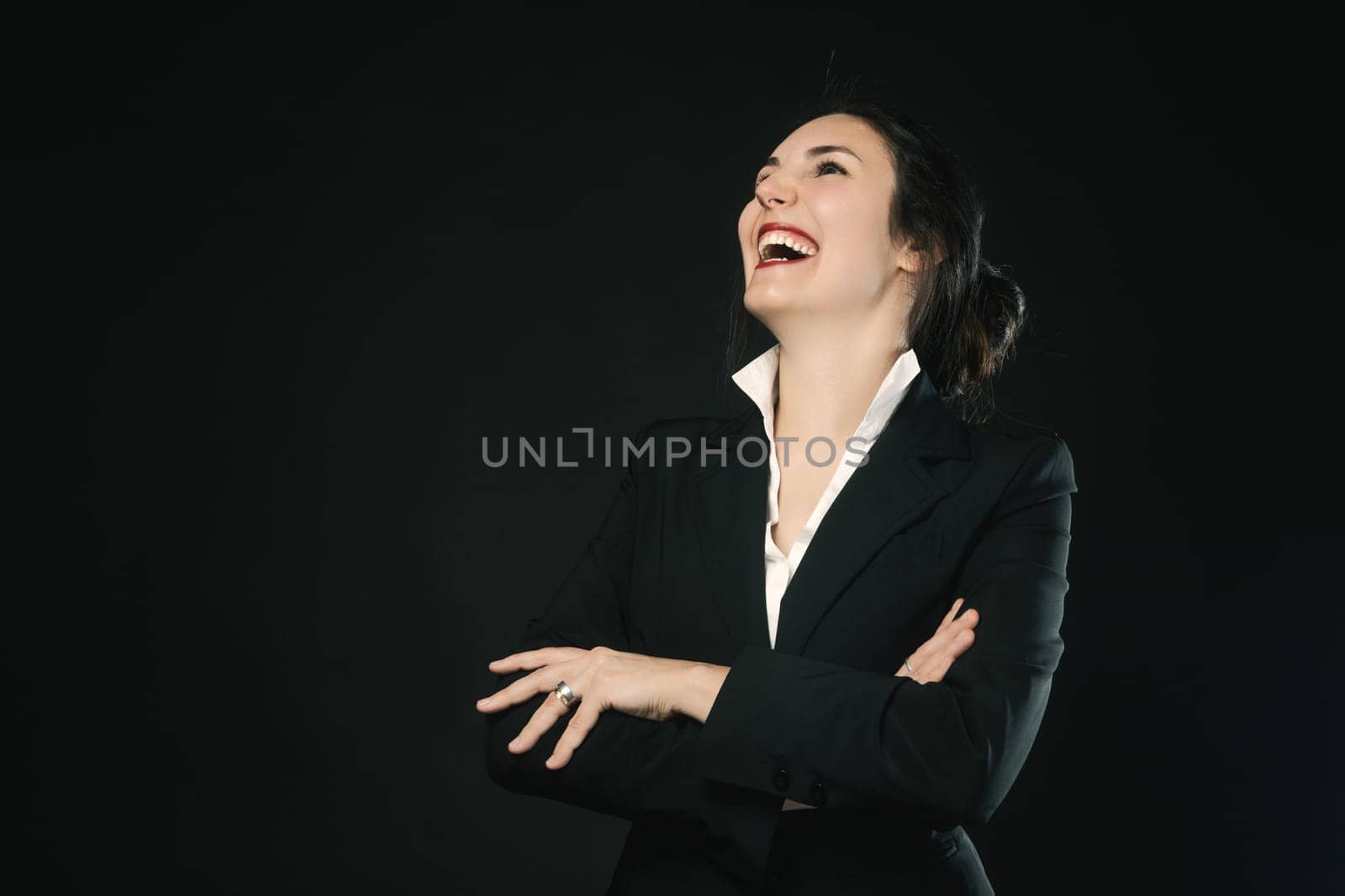 Woman with tied-back hair, in black business dress, laughing against a black backdrop. Her competence is evident, her value undeniable, and her beauty is still alive. She enjoys a joyful moment before