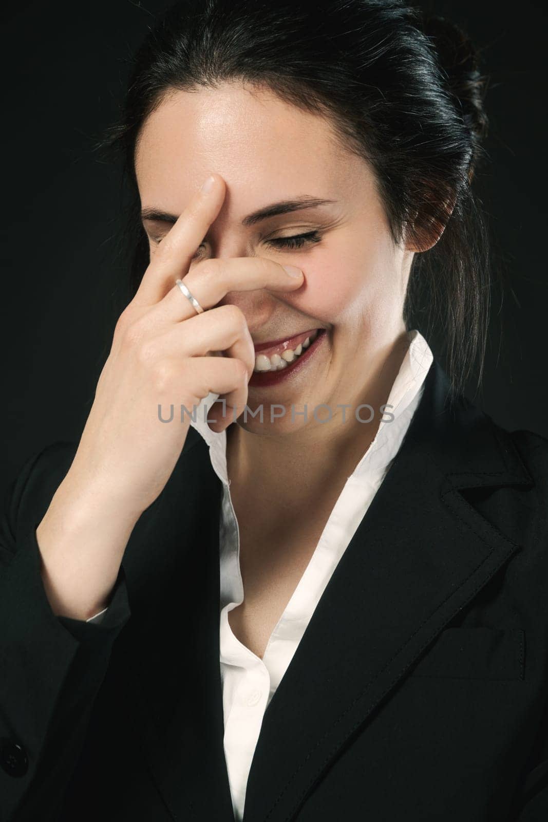 laughing woman in black business attire against a black background. Proven skill, evident value, and enduring beauty. Responsible for her happiness, she savors a joyful moment before reentering life's