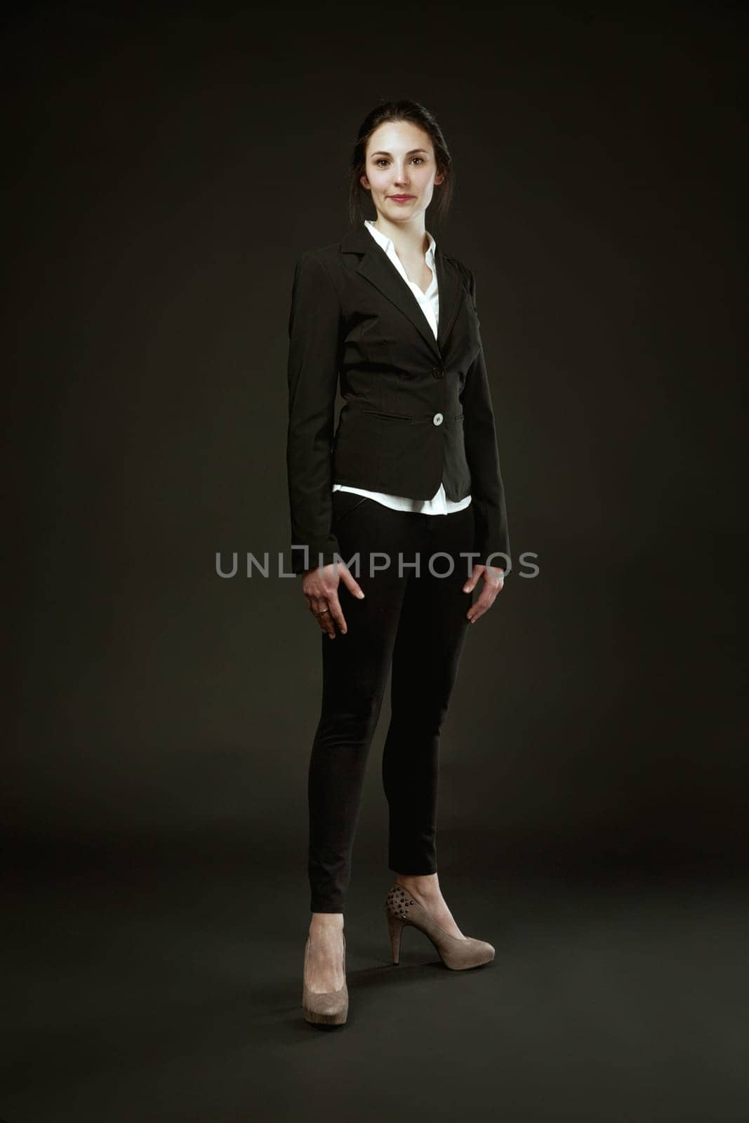 woman in a black suit stands proudly against a black background. Choosing high heels not for male approval, but for her own self-recognition of beauty