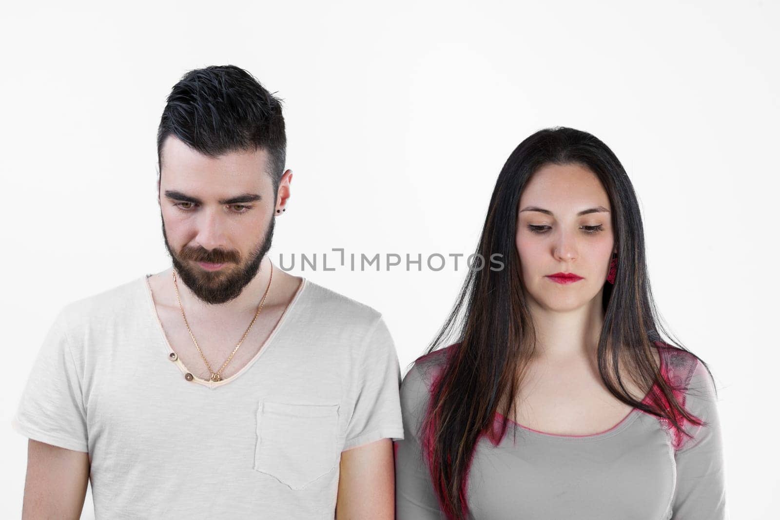 Man and woman stand side by side, showing no expression or perhaps sadness. Facing issues or crisis in their relationship, feeling life's impact. He bears a beard, she long black hair