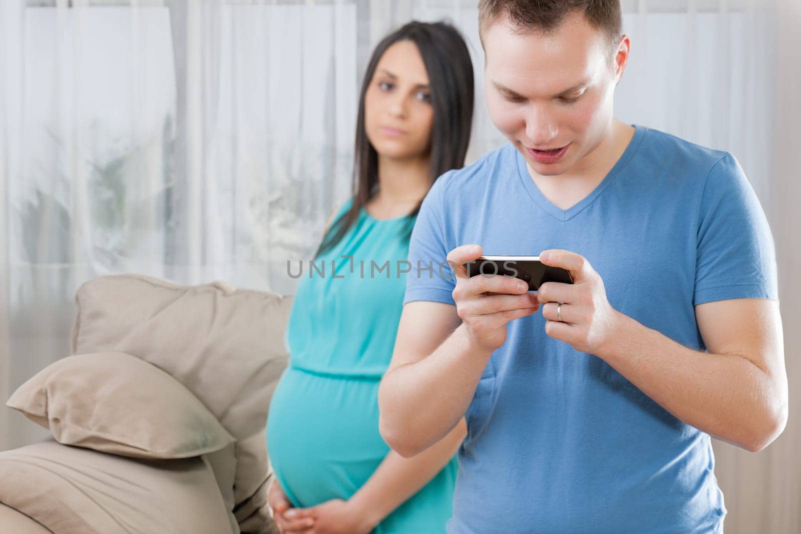 Pregnant young woman observes a man engrossed in games on his phone, reflecting the important responsibility of choosing a partner and creating a life amid limited experience