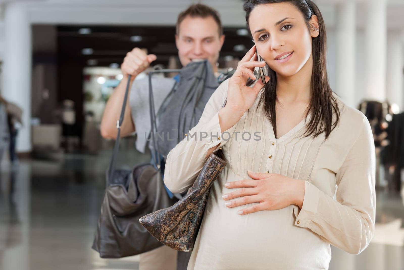 Husband carries bags, following his pregnant wife as she talks on the phone, oblivious. Highlighting the idea of maternity and a dysfunctional relationship