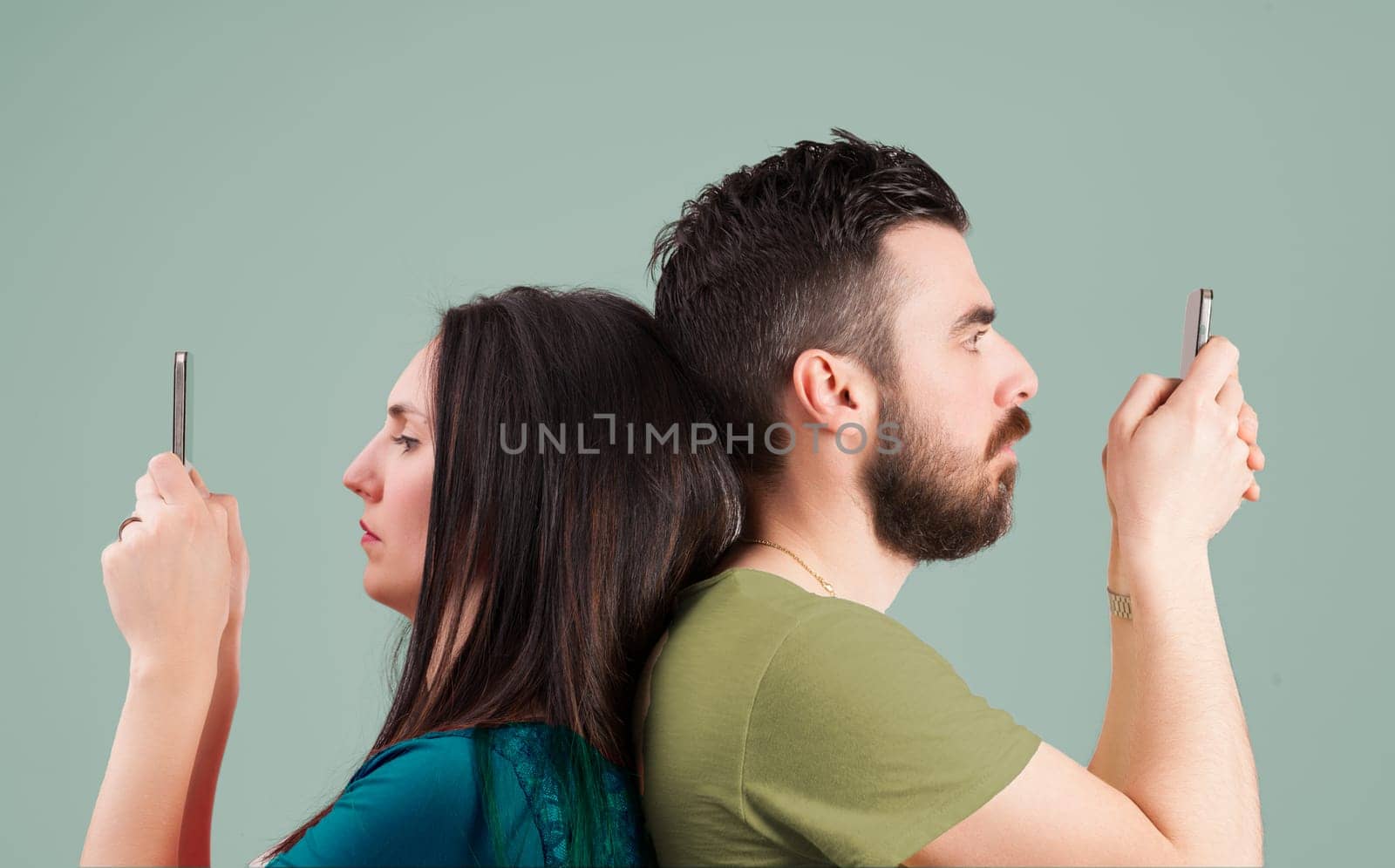 Man and woman, back-to-back, focus on their own screens. Together but apart, they ignore each other, embodying modern separation, engrossed in internet content in simultaneous solitude
