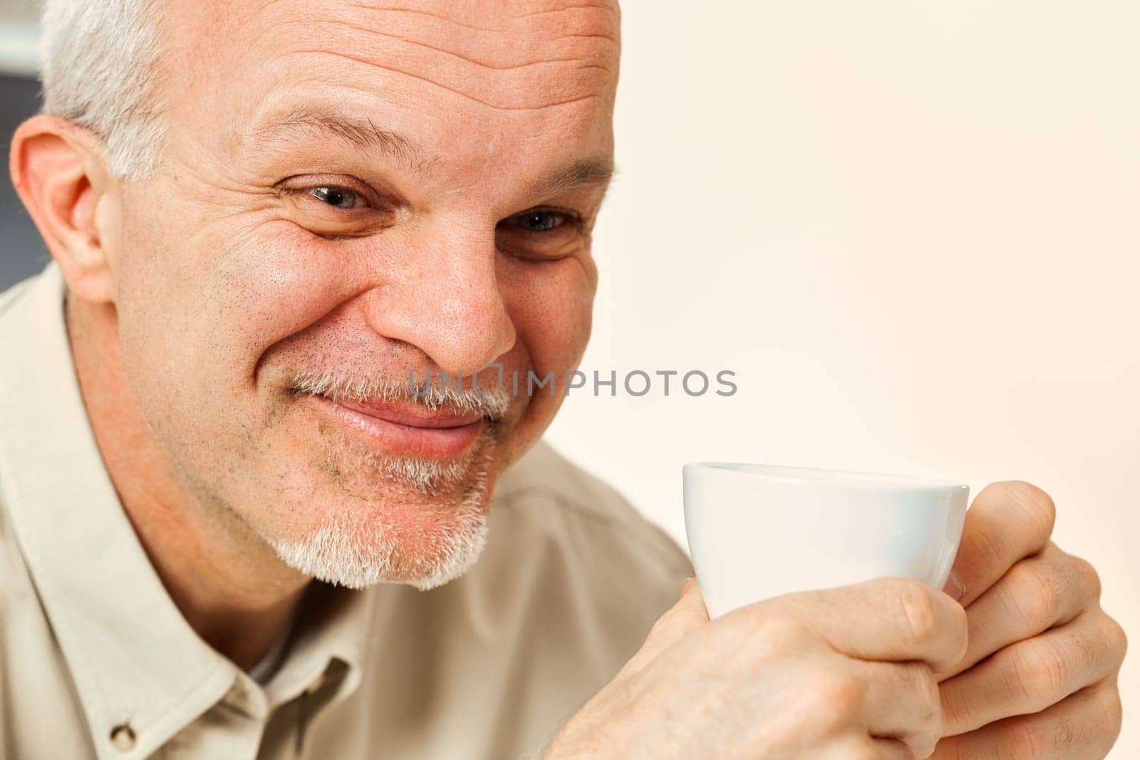 Amidst his thoughts, an aged man tries not to laugh. Holding a drink, likely coffee or tea, he's amused by the notion of something naive or laughable. His seasoned life offers such perspective