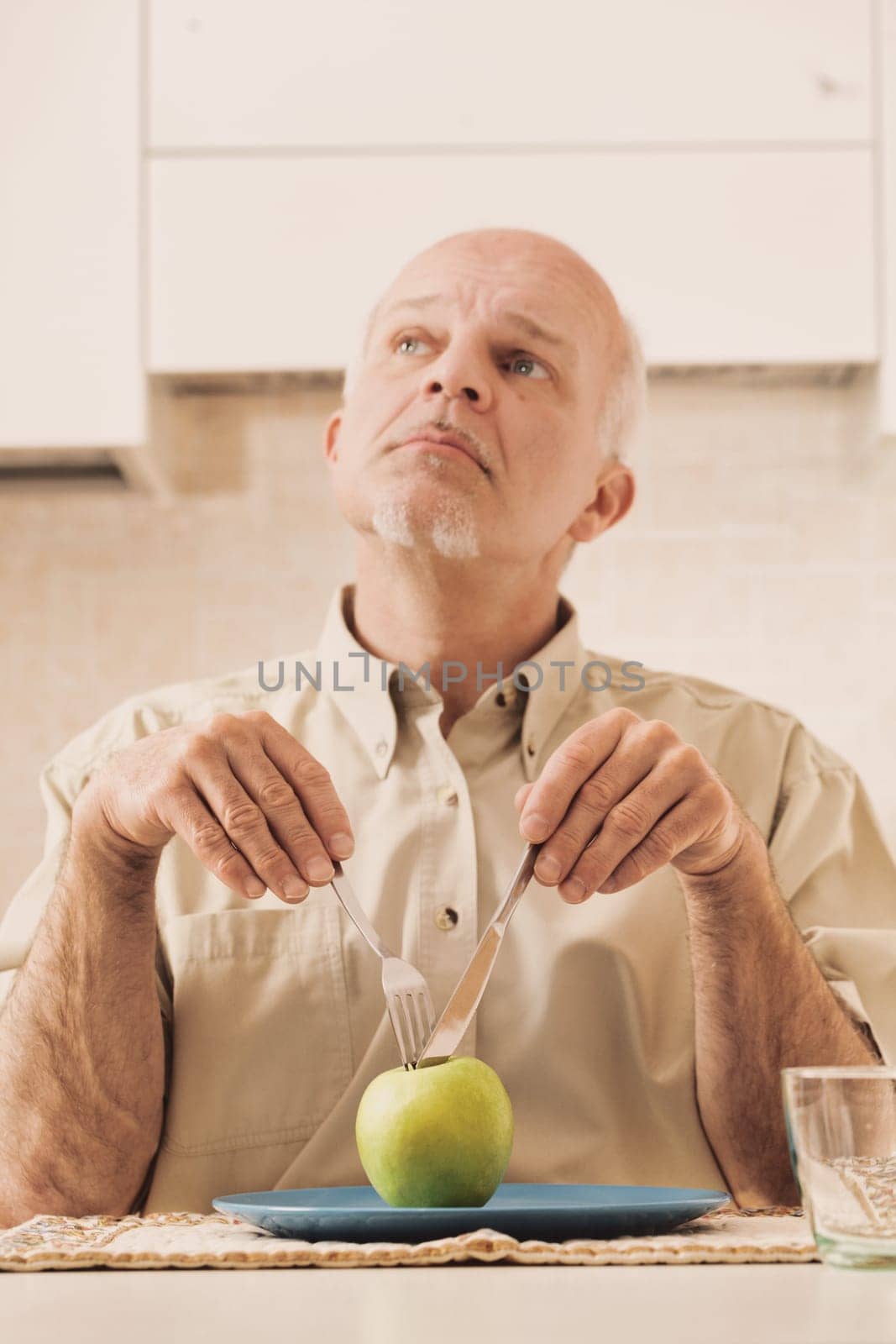 With only a green apple on his plate, an elderly man readies himself, making funny faces. Beneath this facade, he craves delicious foods filled with fats, sugars, and carbs. The doctor's advice? Such