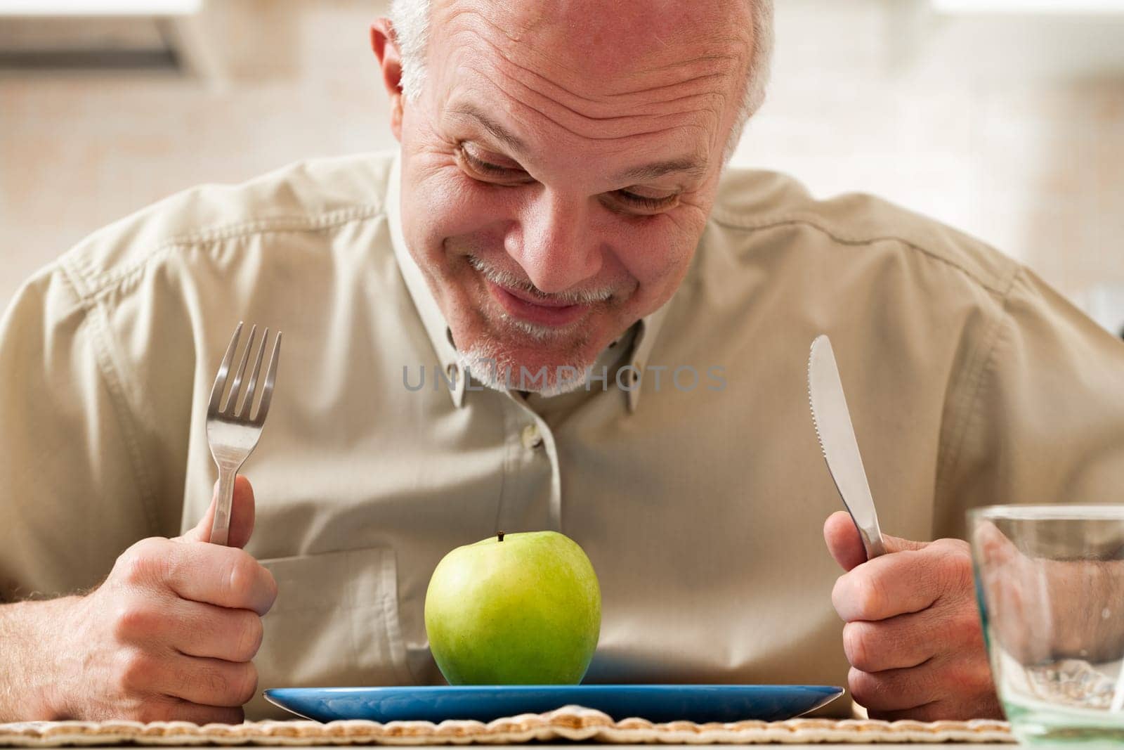 old man stoically prepares to eat just a green apple. It's the only item on his plate, with utensils on the side. His humorous expressions mask a deep desire for rich, fatty, sugary, salty, and carby