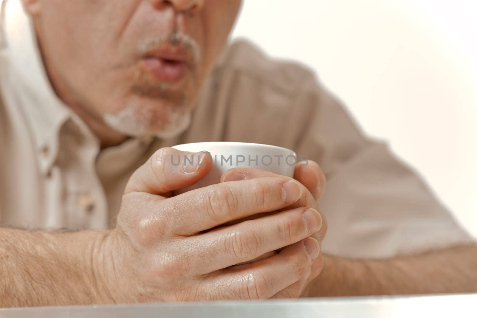 Amidst the cold embrace of a winter morning, the sun offers little relief. An aged man with an unrecognizable face tightly holds his coffee, blowing on it to cool. It's a delicate balance between warm