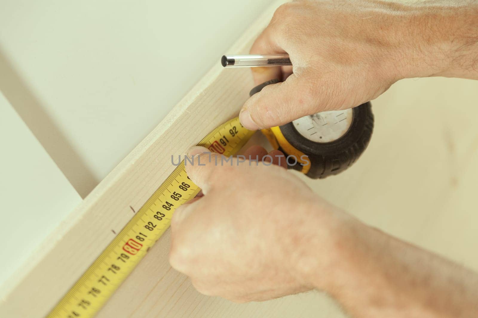 Close-up detail of a carpenter's tape measure as he measures a piece of wood that he will later use in his woodworking workshop