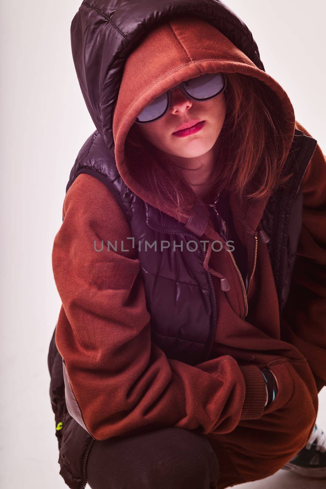 Showcasing a casual, yet edgy fashion sense, the woman squats while donning a hooded jacket and stylish sunglasses