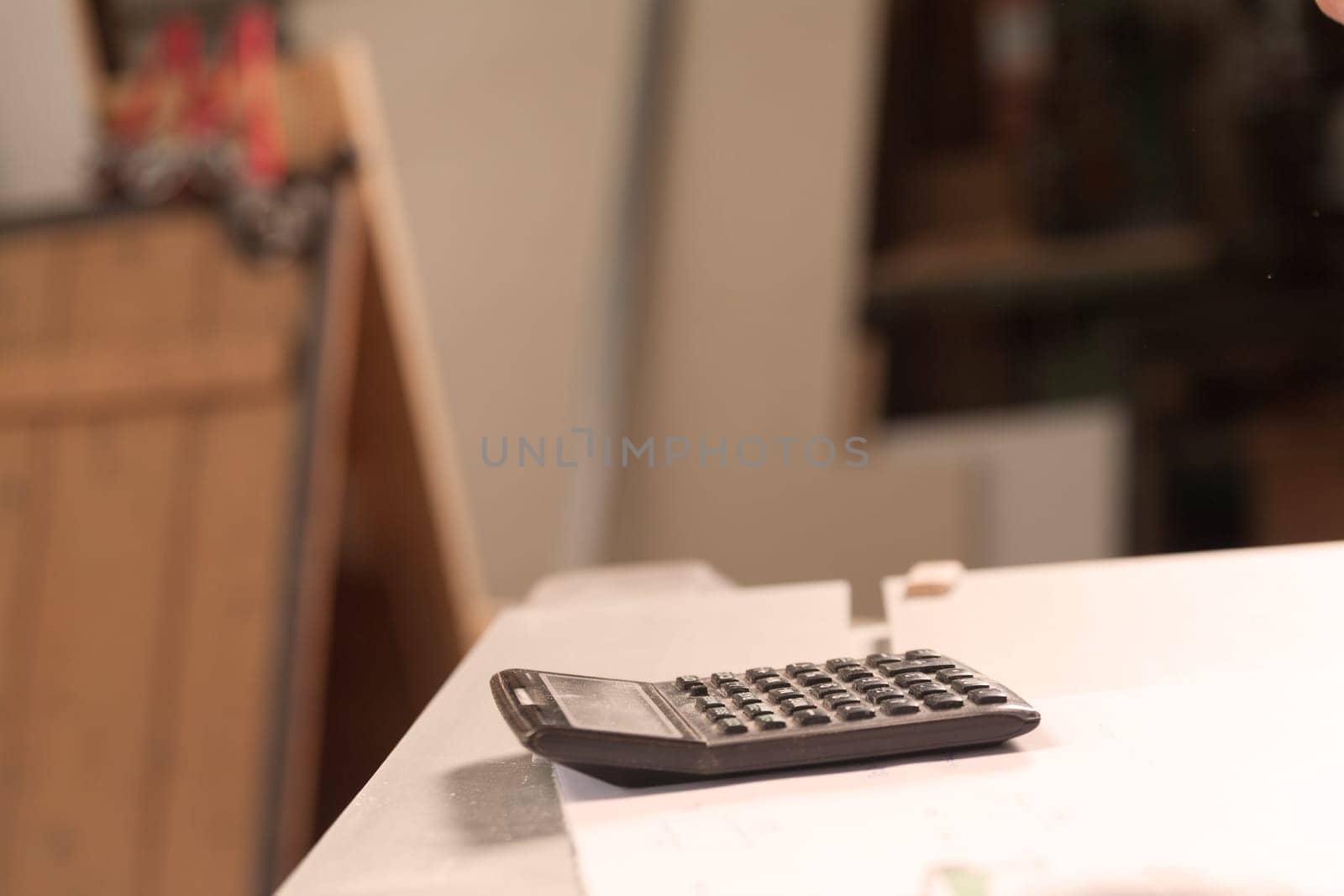 calculator in the foreground resting on a table full of papers, the rest is blurry, the calculator is all smeared with sawdust